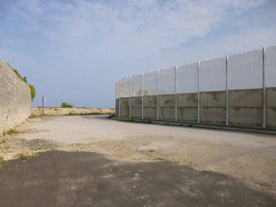 Long, tall metal fence along the edge of a paved lot